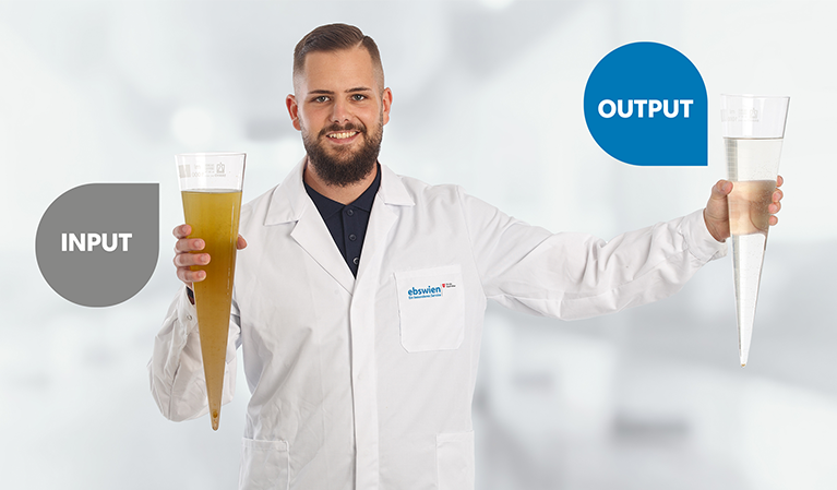 Mitarbeiter der ebswien im Labormantel zeigt zwei Imhof-Trichter, von denen je einer mit Rohabwasser und mit gereinigtem Abwasser gef&uuml;llt ist. &copy; Christian Houdek